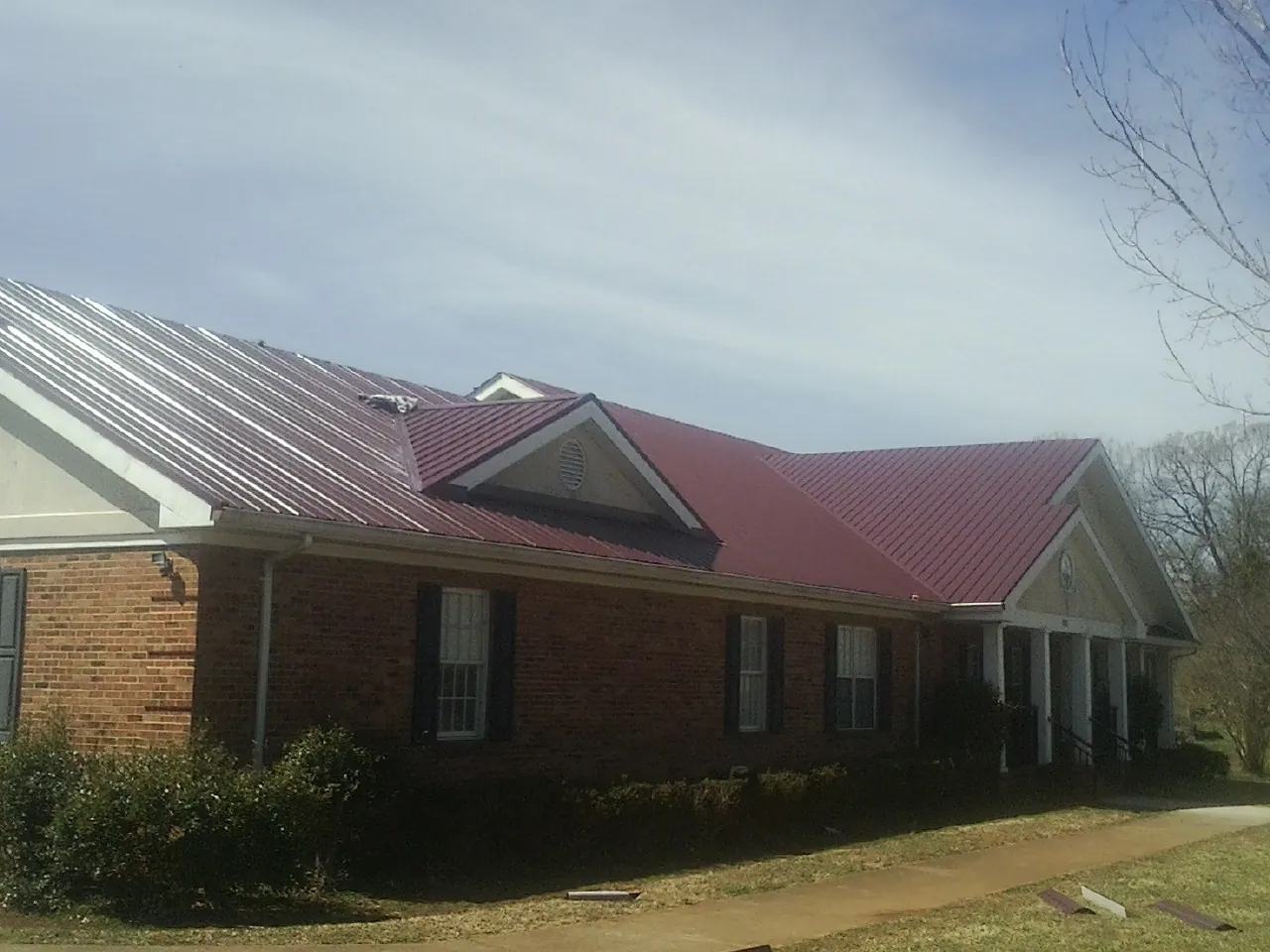 Red metal roof with gabled entries on a long brick building, from a Hail Damage Roof Repair job in Galena