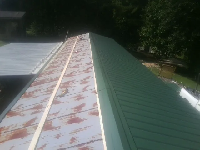Old rusted panels beside newly installed green metal roofing — Wind Damage Roof Repair by Roofing Brothers in Galena