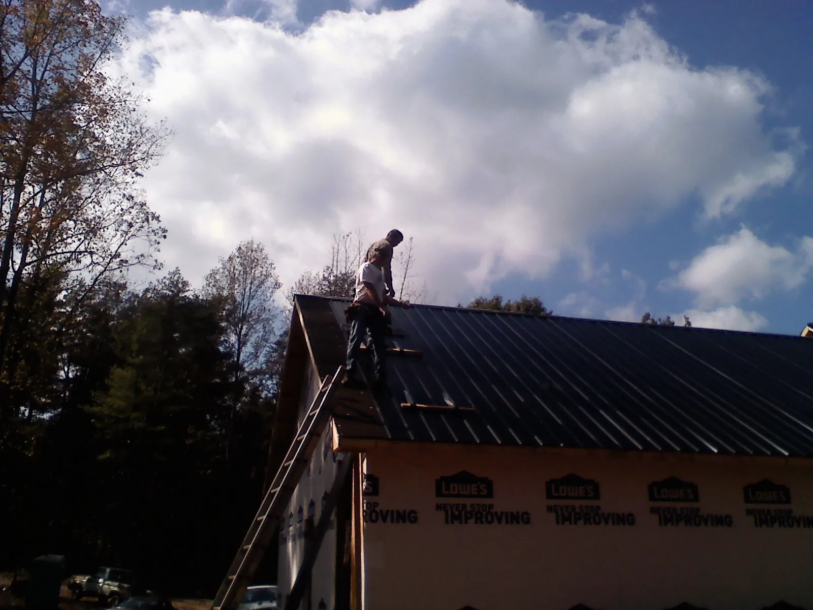 Roofer fastening dark metal panels high against a cloudy sky, from a Roof Inspection job in Galena